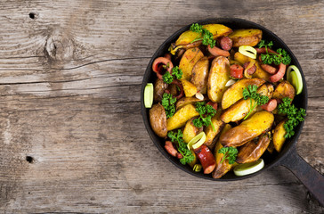 Fried potatoes with sausages on old wooden table
