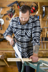 Carpenter sawing wood with hand saw in workshop