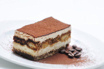 Tiramisu cake with cocoa powder and coffee beans on white plate, photography for patisserie, sponge cake