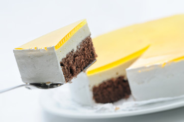 cocoa sponge cake with yellow gelatin on metal spoon, tart on white plate, patisserie, photography for shop, birthday cake