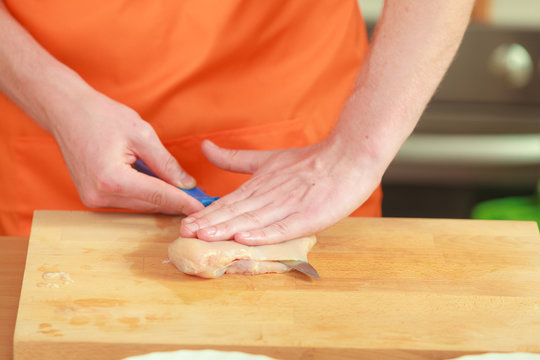 Man cutting raw chicken meat on wooden board