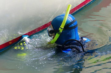 Scuba diver with snorkel and aqualung tank is cleaning a boat hull with a scrubbing pad removing all organic growth so the hull is smooth & clean resulting in higher speeds and better fuel efficiency