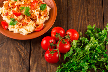 Fettuccine pasta with shrimp tomatoes and herbs. wooden background