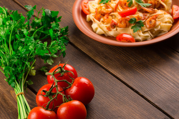 Fettuccine pasta with shrimp tomatoes and herbs. wooden background