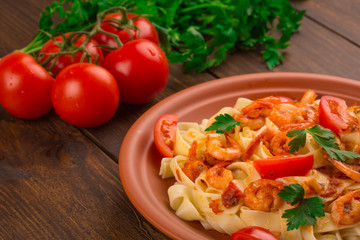 Fettuccine pasta with shrimp tomatoes and herbs. wooden background