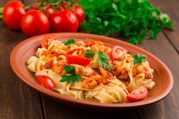 Fettuccine pasta with shrimp tomatoes and herbs. wooden background