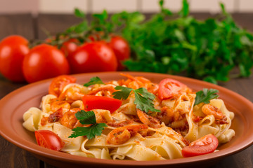 Fettuccine pasta with shrimp tomatoes and herbs. wooden background