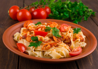 Fettuccine pasta with shrimp tomatoes and herbs. wooden background
