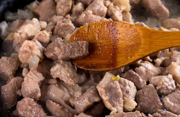 a piece of roasted meat for goulash on wooden spoon