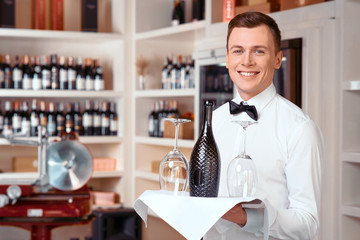 Pleasant sommelier holding tray with wine bottle