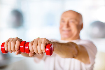 Positive senior man practicing with weights 