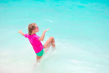 Fototapeta na wymiar Adorable little girl splashing in tropical shallow water during summer vacation