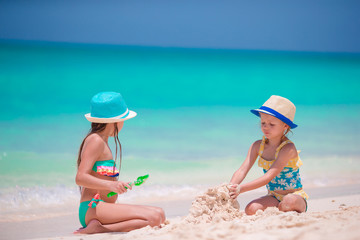 Happy little girls playing on beach sand during tropical vacation