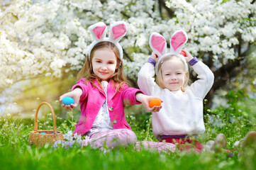 Two adorable little sisters hunting for easter egg in blooming spring garden