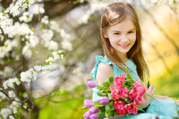 Adorable little girl holding tulips for her mother in blooming cherry garden