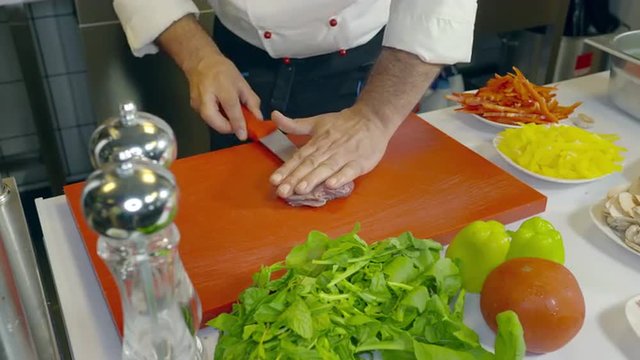 Close-up of adult male chef cutting and slicing fresh meat