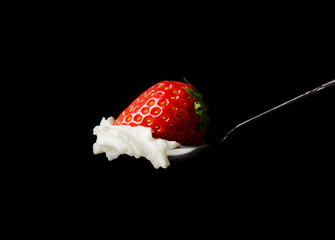 Whipped cream and a strawberry in a silver spoon on black backgr