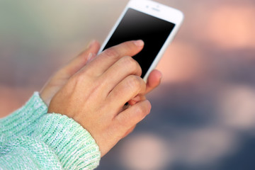 Female hands holding a mobile phone outdoors, on blurred background
