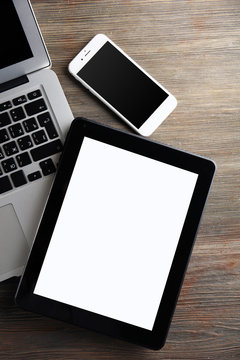 An open silver laptop, mobile phone and modern tablet on the wooden background
