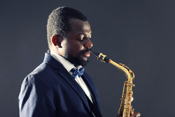 African American jazz musician playing the saxophone on grey background