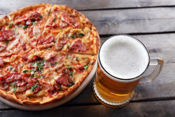 Tasty pizza and glass of beer are on wooden table, close up