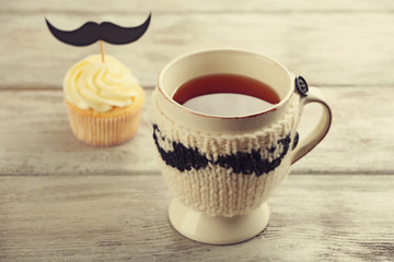 Delicious creative cupcake with mustache and cup of tea on wooden table