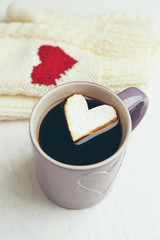 Cup of hot coffee with heart marshmallow and warm mittens on light wooden background, close up