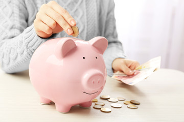 Woman putting euro coin and banknotes into a piggy bank on the table. Financial savings concept