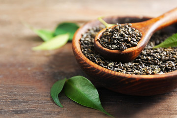 Granulated tea with green leaves in wooden bowl on table closeup
