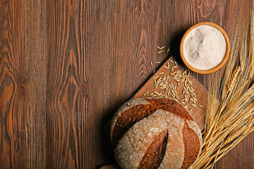 Fresh baked bread, a bowl of flour and wheat ears on the wooden background