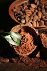 Bowl with aromatic cocoa powder and green leaf on wooden background, close up