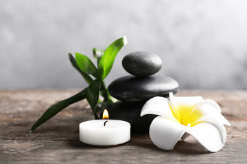 Obraz na płótnie Canvas Spa stones with candle, bamboo and tropical flower on wooden table against grey background