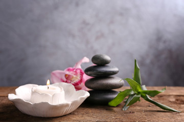 Fototapeta na wymiar Spa stones with bamboo, pink orchid and candle on wooden table against grey background