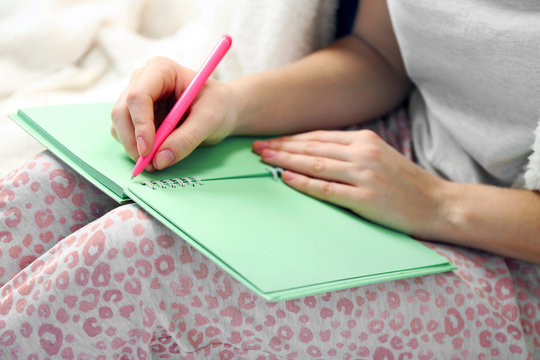 Woman in pajamas writing diary on her bed