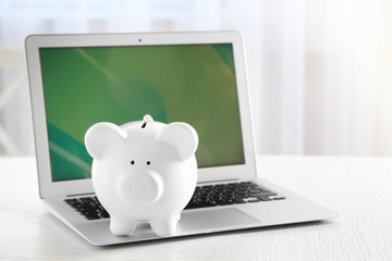 Piggy bank with laptop on table indoors