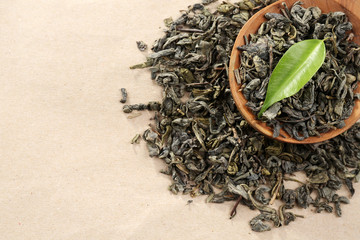 Scattered tea with green leaves in wooden spoon on burlap background