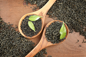 Scattered tea with green leaves in wooden spoons on table background