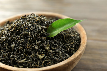 Dry tea with green leaves in bowl on wooden table background