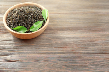 Dry tea with green leaves in bowl on wooden table background, copy space