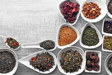 Variety of dry tea in bowls and spoons on grey wooden background, copy space