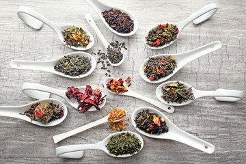 Variety of dry tea in white spoons on grey wooden background