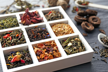 Variety of dry tea in wooden box with spoons on grey background - Powered by Adobe