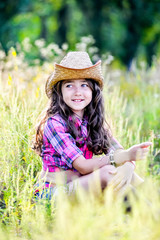 little girl sitting in a field wearing a cowboy hat