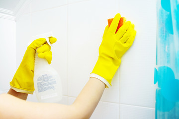 A wooman washer is cleaning tiled surface in bathroom. The girl