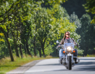 Biker with long hair and beard in sunglasses and leather jacket on the road. Tilt shift lens blur effect
