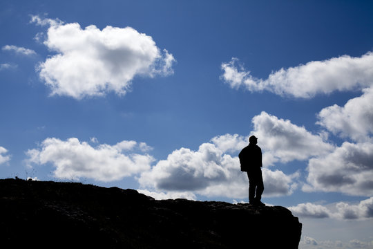 Silueta de hombre mirando las nubes desde acantilado