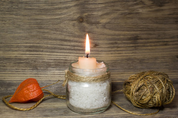Burning white candle in glass jar on wooden background