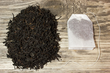 Dry tea leaves for black tea and paper tea bag on wooden background