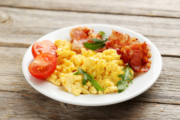 Scrambled eggs with bacon and vegetables on a grey wooden table