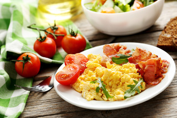 Scrambled eggs with bacon and vegetables on a grey wooden table